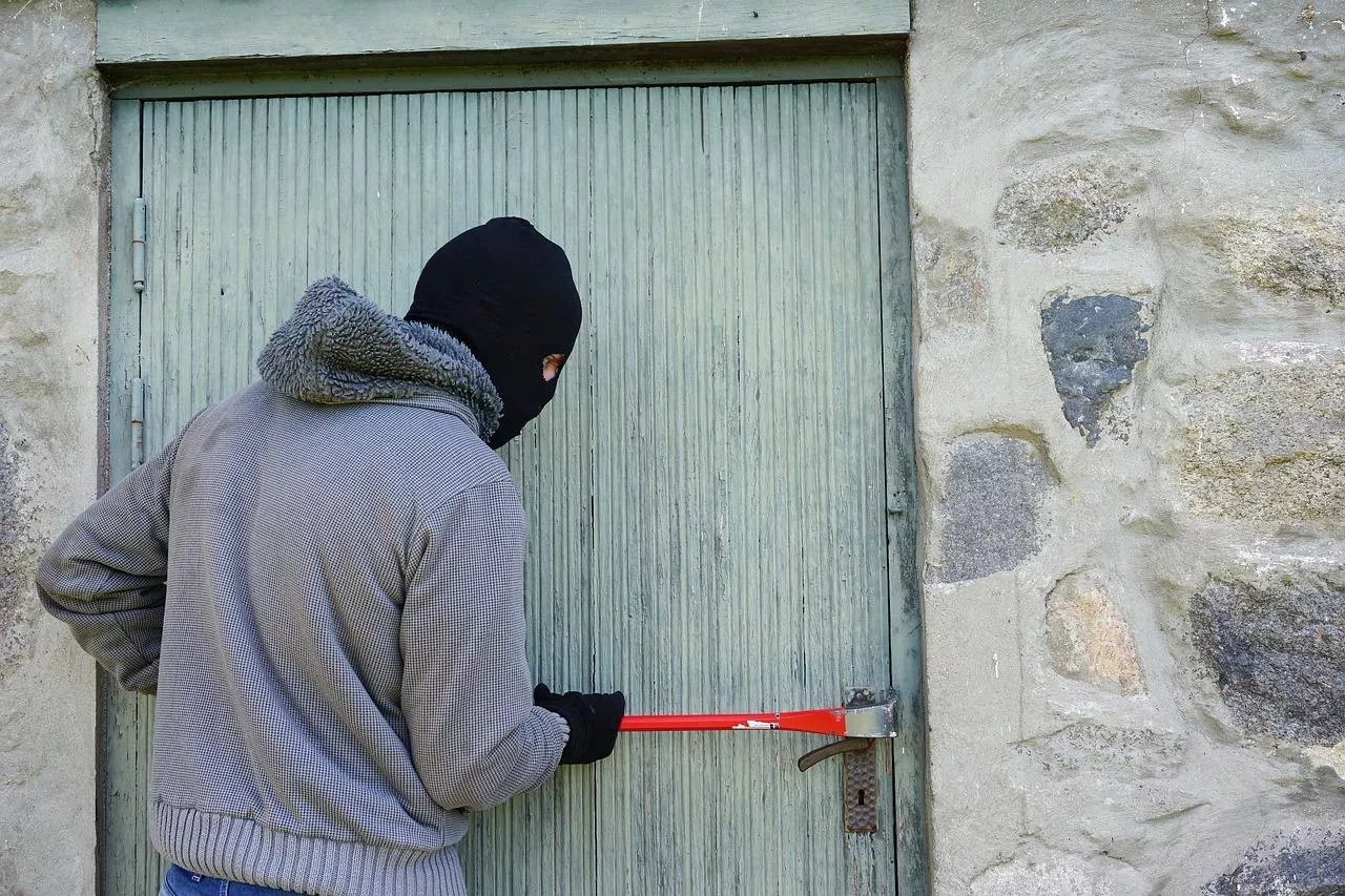 Osoba w kominiarce próbuje wyłamać zamek drzwi łomem.