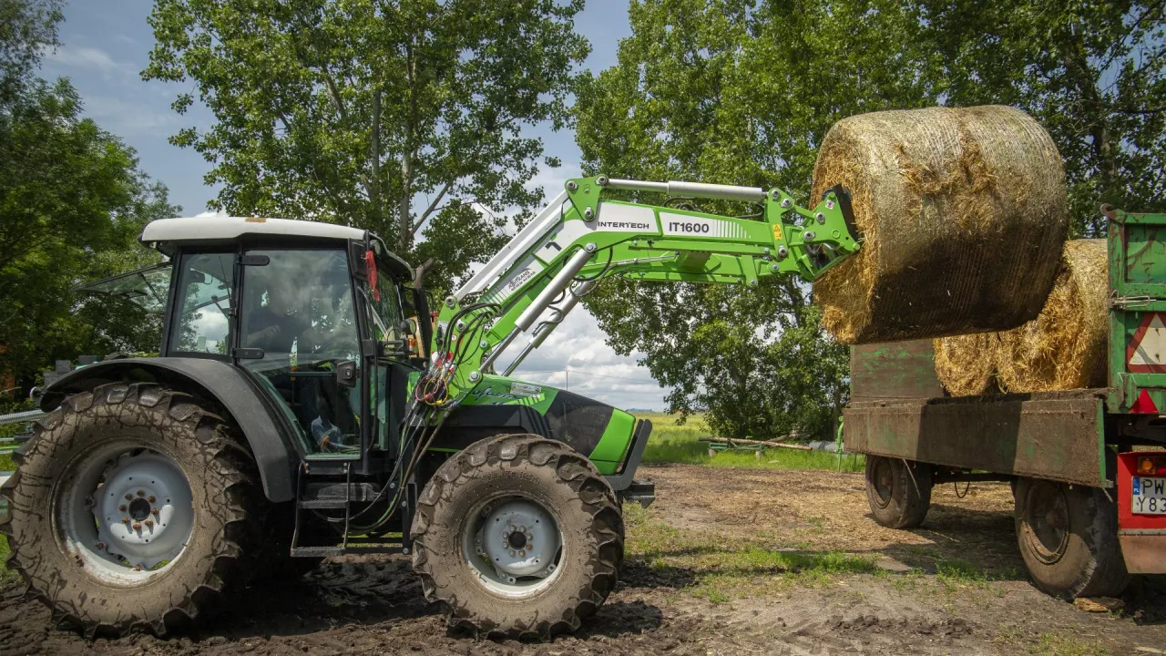 Ładowarcz Intertech IT 1600 z ciągnikiem Deutz Fahr podczas załadunku bel słomy na przyczepę z niewielkiego stogu.