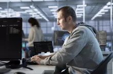 Focused man working in server farm capable of processing vast amounts of data. IT programmer at PC desk typing on keyboard, updating servers controlling network resources